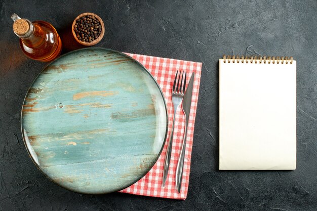 黒のテーブルの上の赤と白の市松模様のナプキンノートの上面図ラウンドプラッターディナーナイフとフォーク