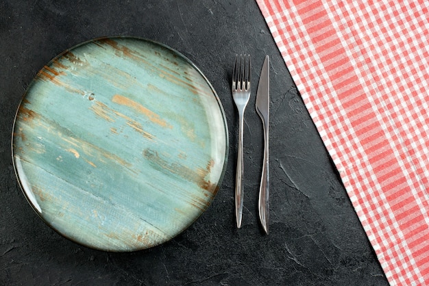 Top view round platter fork and dinner knife red and white checkered tablecloth on black table