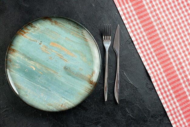 Top view round platter fork and dinner knife red and white checkered tablecloth on black table