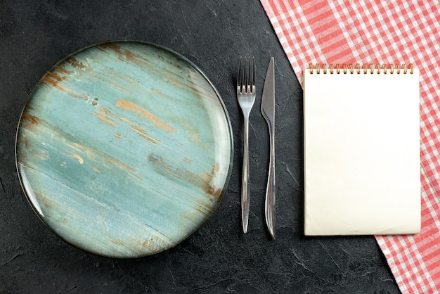 상위 뷰 라운드 플래터 포크와 디너 나이프 빨간색과 흰색 체크 무늬 식탁보 노트북 블랙 테이블에