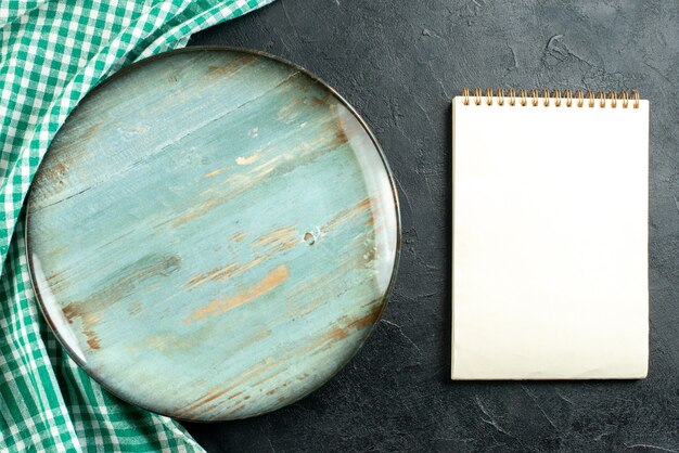 Top view round platter green and white tablecloth notebook on black table