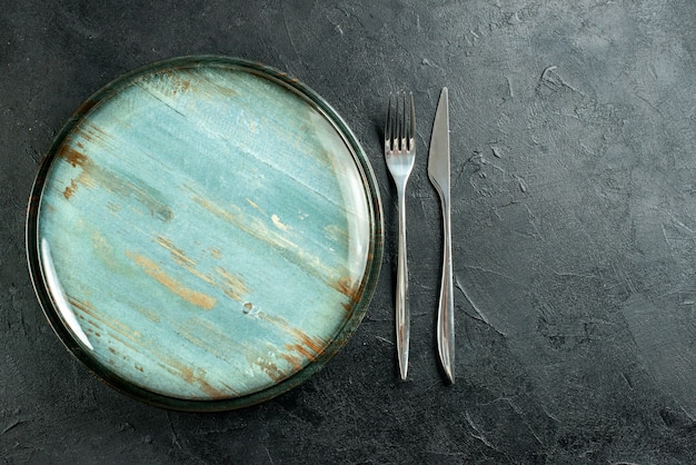 Foto gratuita vista dall'alto piatto rotondo in acciaio forchetta e coltello da cena sul tavolo nero posto libero