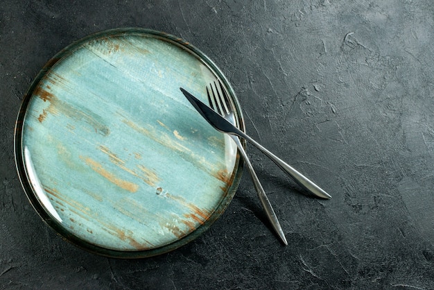 Foto gratuita vista dall'alto piatto rotondo in acciaio forchetta e coltello da cena sulla tavola nera con posto libero