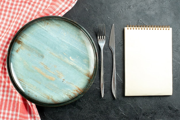 상위 뷰 라운드 플래터 강철 포크와 저녁 식사 칼 블랙 테이블에 빨간색과 흰색 체크 무늬 식탁보 노트북