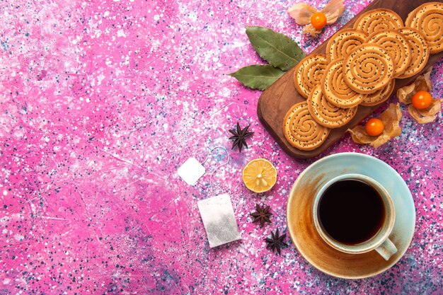 Top view of round sweet cookies with cup of tea on pink surface