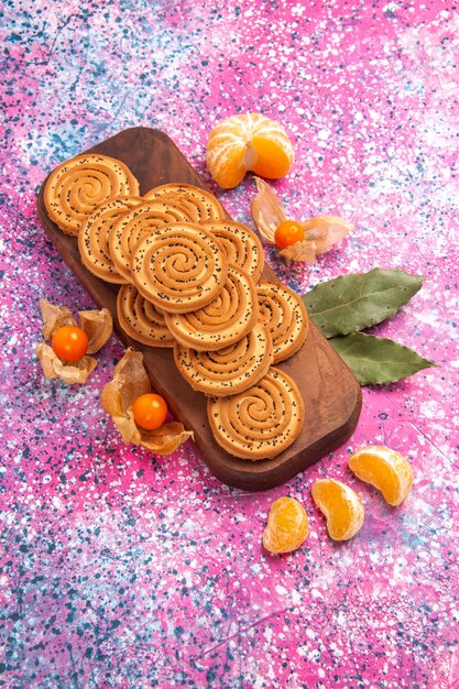 Top view of round sweet cookies with tangerines on the pink surface