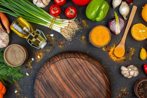 Top view round wooden board black pepper wooden spoon oil bottle garlic green onions turmeric on table