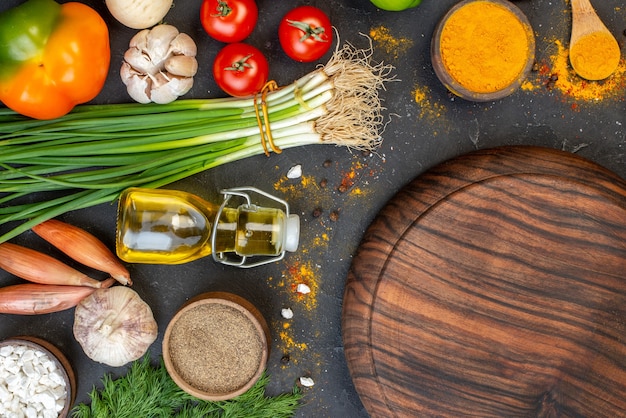 Foto gratuita vista dall'alto tavola di legno rotonda aglio aneto cipolle verdi bottiglia di olio curcuma sale marino sul tavolo