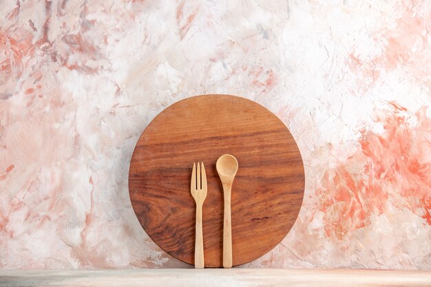 Top view of round wooden chopping board and spoons standing on colorful wall