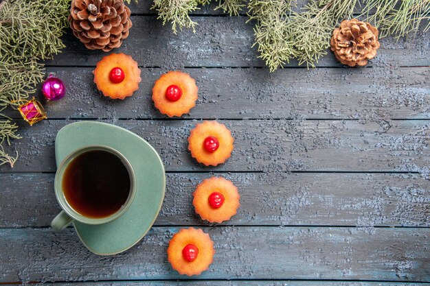 Вид сверху округлые вишневые кексы еловые ветки рождественские игрушки конусы и чашка чая на темном деревянном столе с копией пространства
