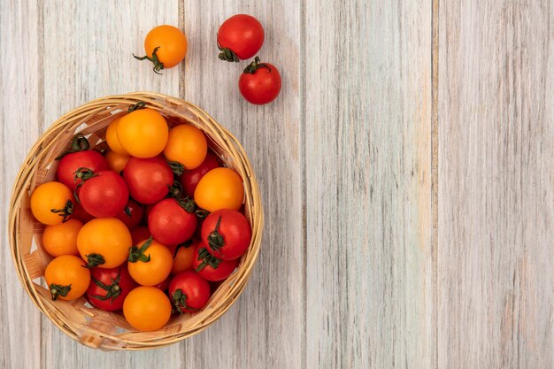 Top view of rounded red and orange tomatoes on a bucket on a grey wooden wall with copy space