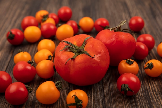 Top view of rounded red tomatoes with orange and red cherry tomatoes isolated on a wooden surface
