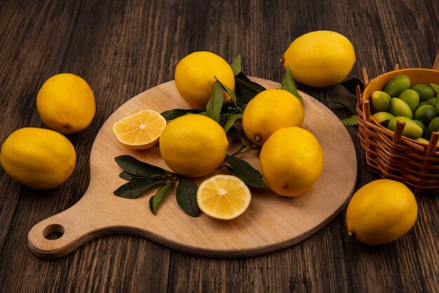 Top view of rounded shape lemons isolated on a wooden kitchen board with kinkans on a bucket on a wooden background