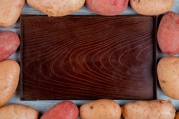 Top view of russet and red potatoes set in square shape around empty tray on wooden surface