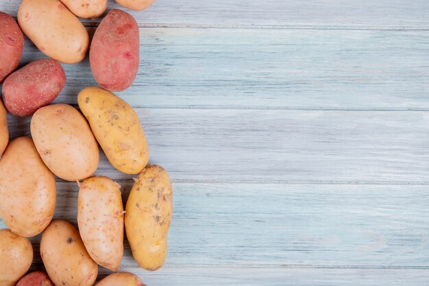 Top view of russet white yellow and red potatoes on left side and wooden surface with copy space