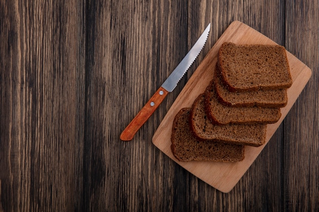 Вид сверху ломтиков ржаного хлеба на разделочной доске и ножом на деревянном фоне с копией пространства