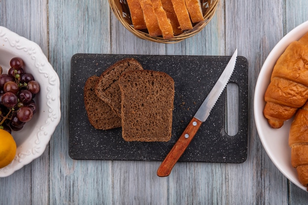 木製の背景にライ麦パンのスライスとクロワッサングレープネクタコットとまな板の上のナイフのトップビュー
