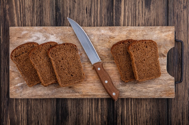 Top view of rye bread slices and knife on cutting board on wooden background