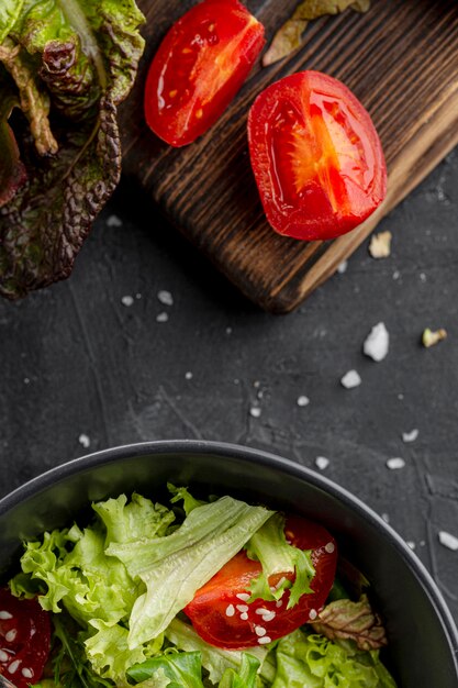 Top view salad in dark bowl next to sliced tomato