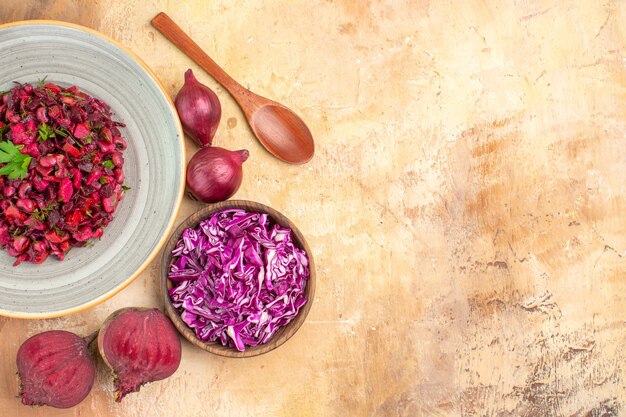 Top view salad on gray plate with green leaves mix vegetables with red onions beetroots and chopped cabbage on a wooden table with free space