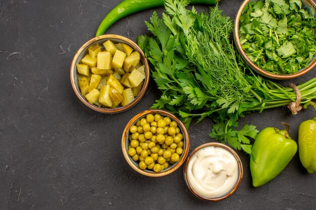 Top view of salad ingredients with greens on dark surface