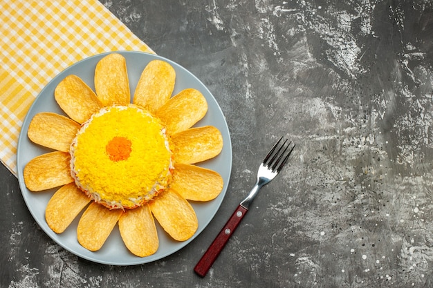 Top view of salad on the left-middle side with yellow napkin under it and fork on side on dark grey background