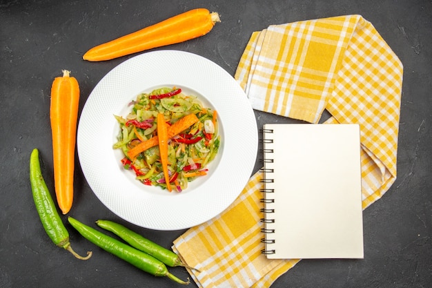 Top view of salad plate of salad with vegetables tablecloth hot peppers white notebook