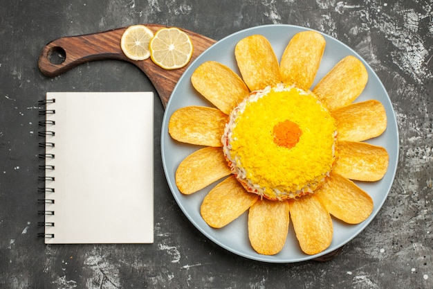 Free photo top view of salad on plate stand with lemon and notepad on side on dark grey table