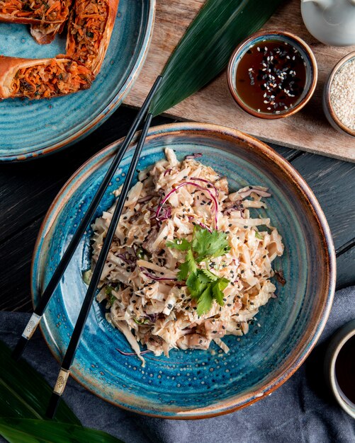 Top view of salad with chopped cabbage chicken and black seeds in a plate with chopsticks on wood