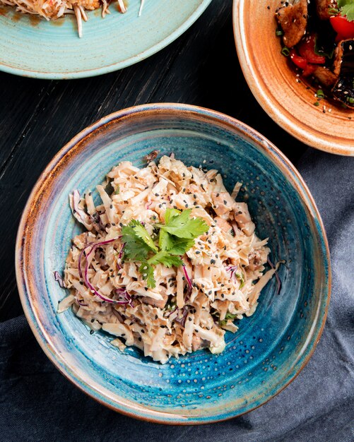 top view of salad with chopped cabbage chicken and black seeds in a plate on wooden surface