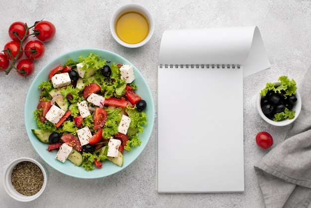 Top view salad with feta cheese, tomatoes and olives with blank notepad