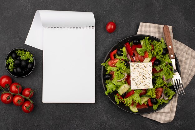 Top view salad with feta cheese and tomatoes with blank notepad