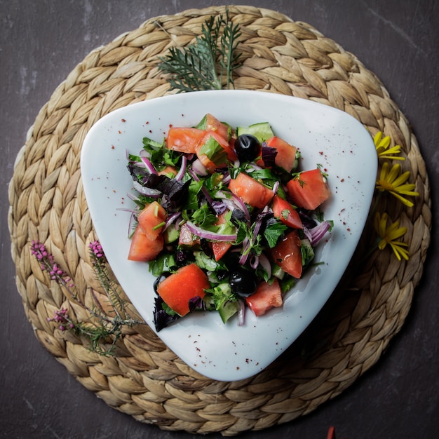 トマト、キュウリ、レタス、玉ねぎ、枝編み細工品スタンドの白いプレートにオリーブの上面サラダ