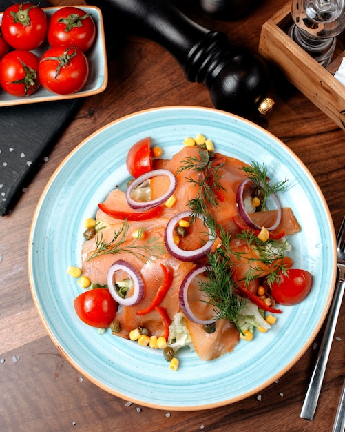 Top view of salmon salad with red onions cabbage and corns topped with dill in a plate on wooden table