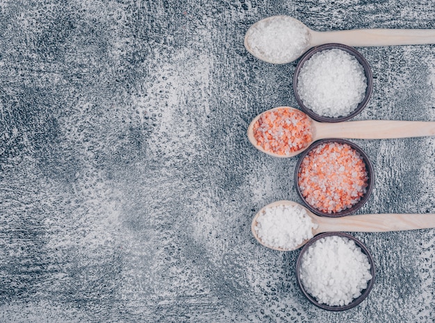 Top view of salt in bowls and wooden spoons with himalayan salt