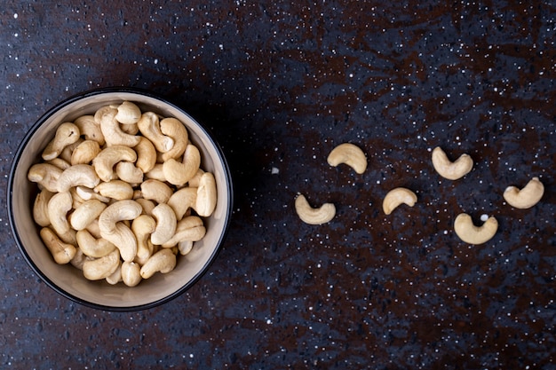 Top view of salted roasted pistachios in a bowl on black background with copy space