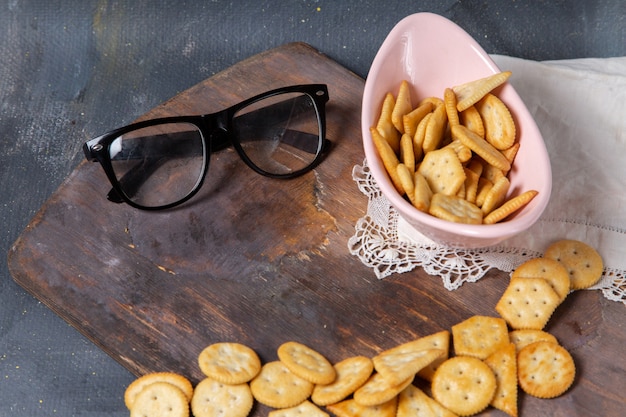 Вид сверху соленые вкусные крекеры с солнцезащитными очками на деревянном столе и сером фоне закуска хрустящие крекеры фото