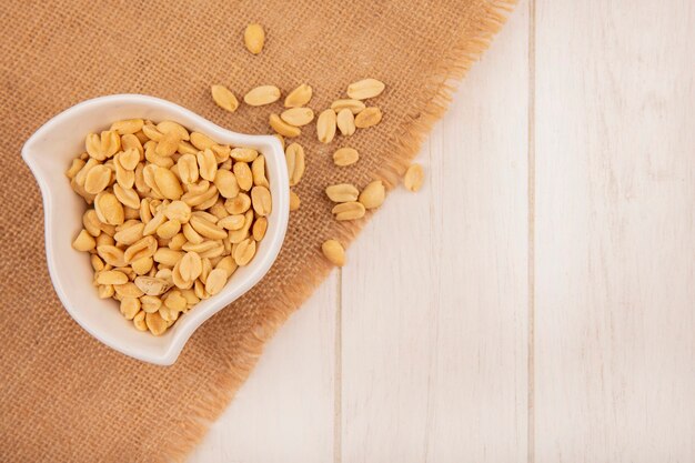 Top view of salty pine nuts on a bowl on a sack cloth on a beige wooden table with copy space