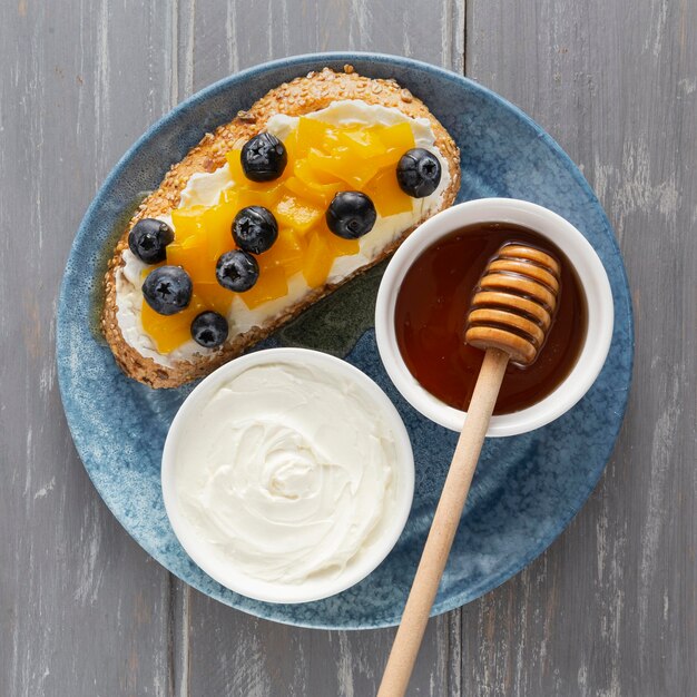 Top view sandwich  with cream cheese and fruits on plate with honey