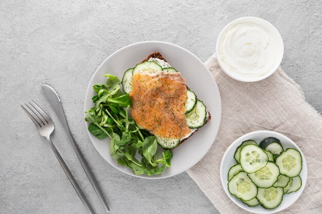 Top view sandwich with cucumbers and salmon on plate with cutlery