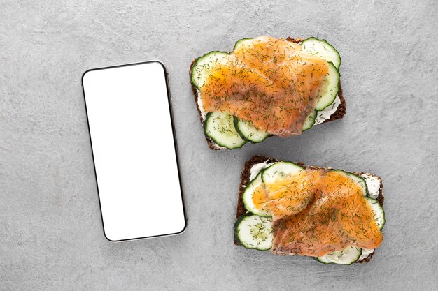 Top view sandwiches with cucumbers and salmon with blank phone