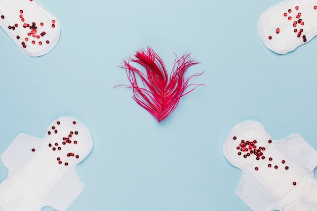 Top view sanitary towel with red sequins and feather