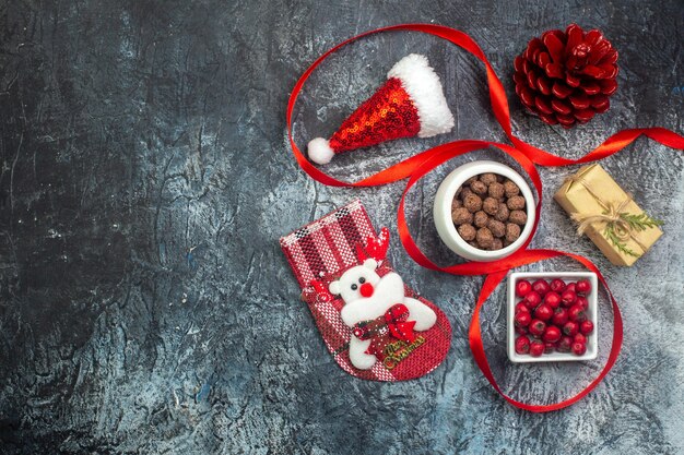 Top view of santa claus hat and cornel chocolate new year sock red conifer cone on the left side on dark surface