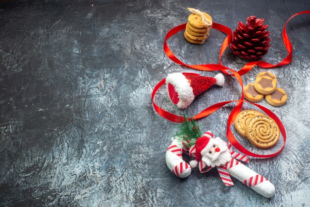 Top view of santa claus hat red conifer cone and various cookies biscuits on the left side on dark surface