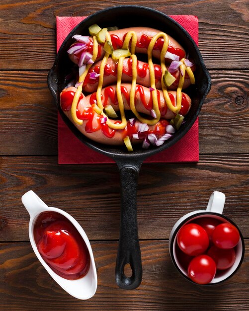 Колбаски на сковороде с соусами и помидорами черри вид сверху