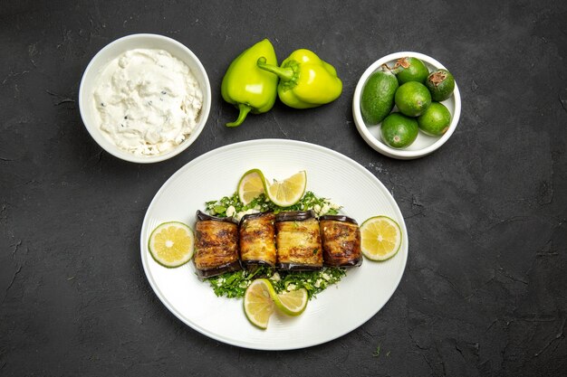 Top view savory eggplant rolls cooked dish with lemon slices and feijoa on dark surface dinner oil cooking meal dish