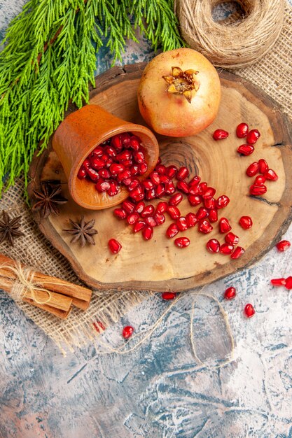 Top view scattered pomegranate seeds in bowl on tree wood board straw thread cinnamon anise seeds on blue-white background