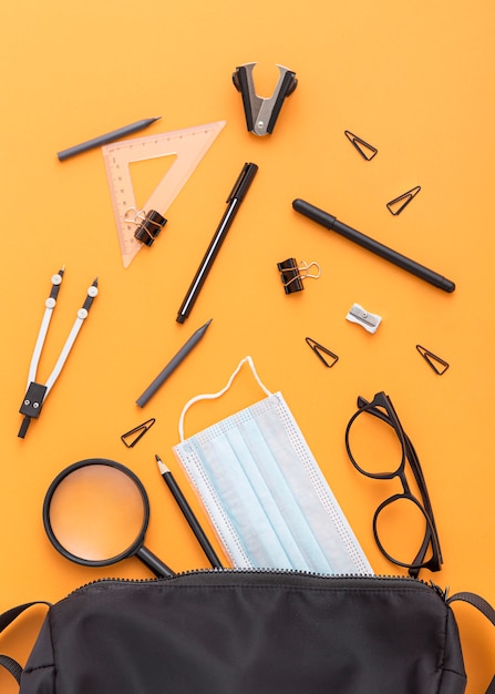 Top view of school supplies with face mask and magnifying glass