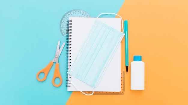 Top view of school supplies with notebook and medical mask