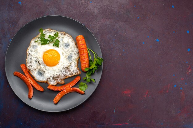 Top view of scrambled eggs with greens and sausages inside plate on dark surface